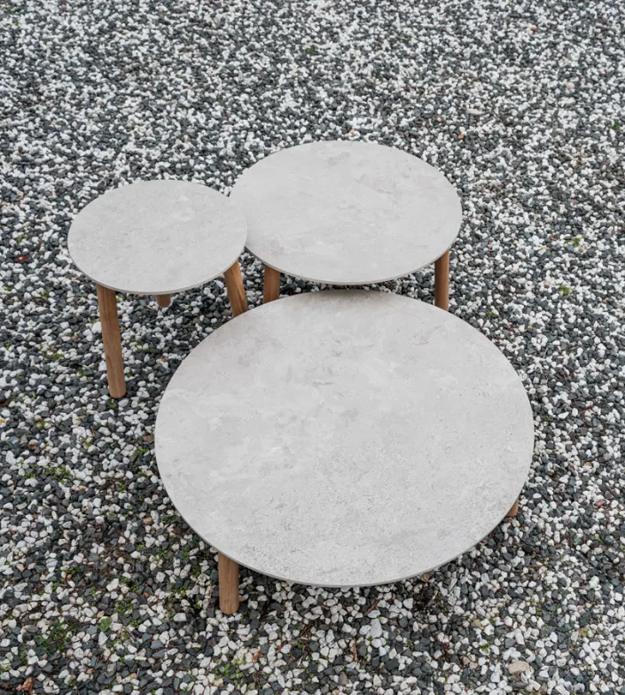 Lento coffee tables and side table by Vincent Sheppard, featuring Sabbia Panna stone tops and solid teak legs, set on a bed of white and grey gravel.